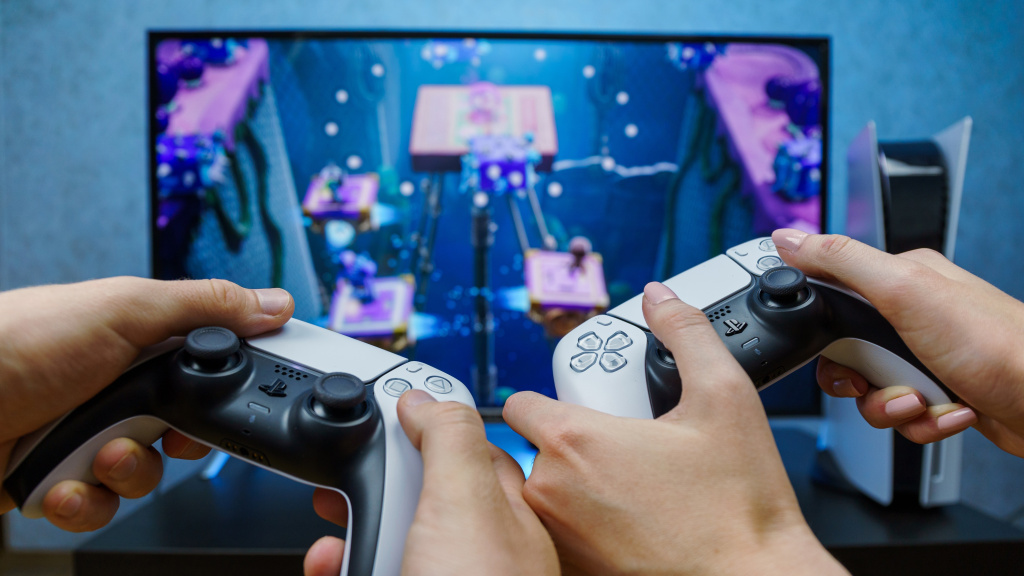 Two people are holding PlayStation joysticks in front of a TV