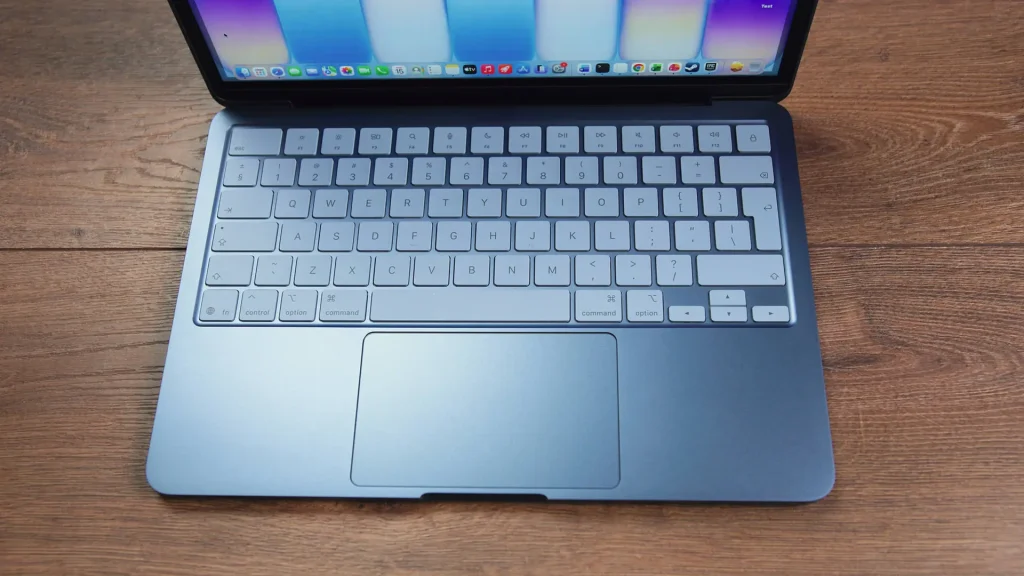 Top-down view of a silver laptop keyboard and trackpad on a wooden desk surface