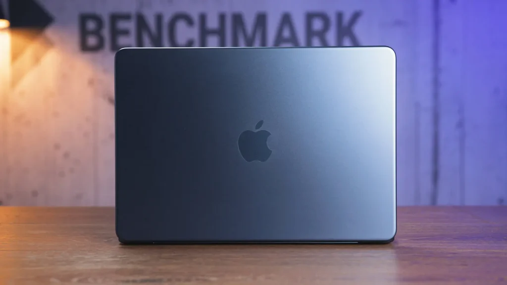 Closed MacBook on a wooden desk with a blue-purple blurred background and visible Apple logo on the lid.