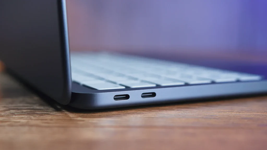 Close-up of a dark laptop's side edge with two USB-C ports resting on a wooden desk.