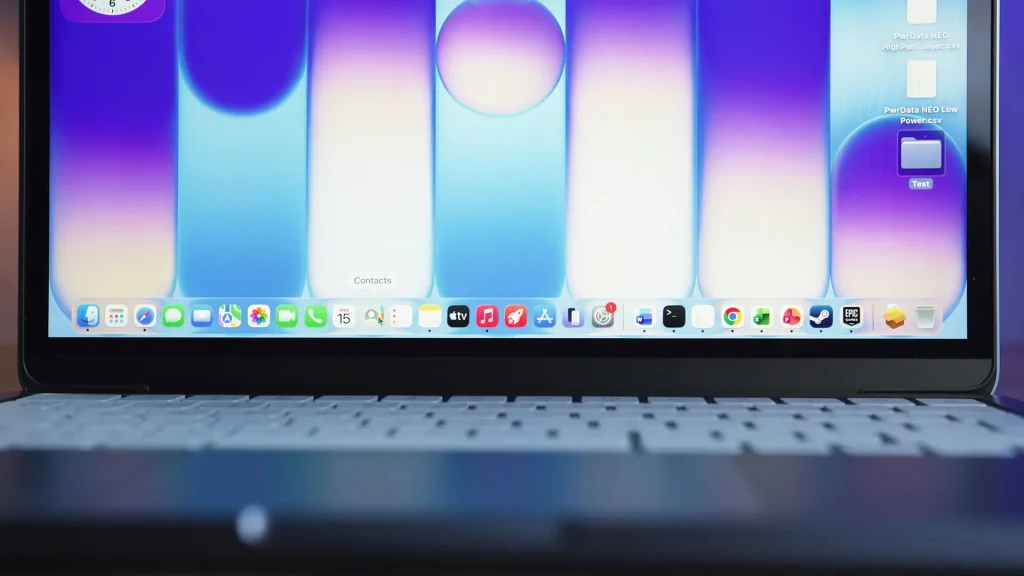 Close-up of a laptop screen showing a colorful gradient wallpaper and the macOS Dock with app icons along the bottom.